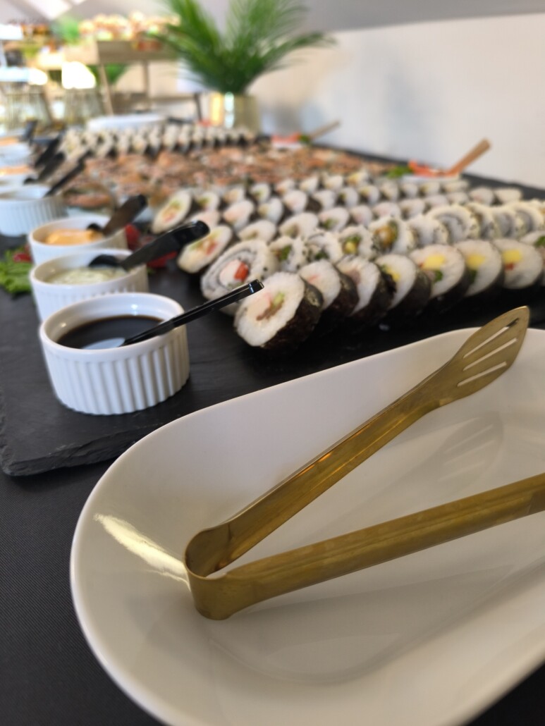 Rolki sushi i złote szczypce na stole bufetowym